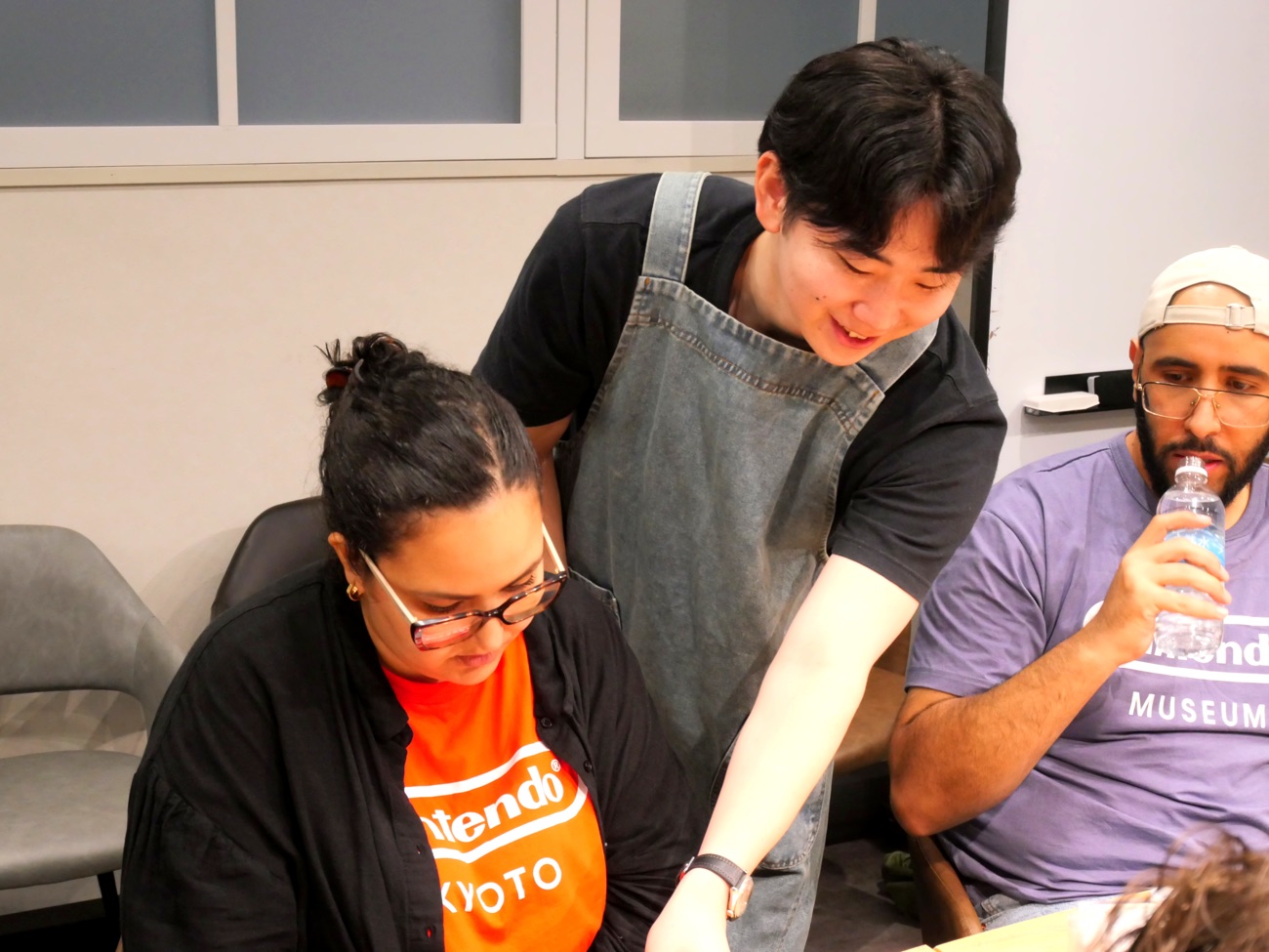 An apron-clad guide leaning in to support a participant during the build