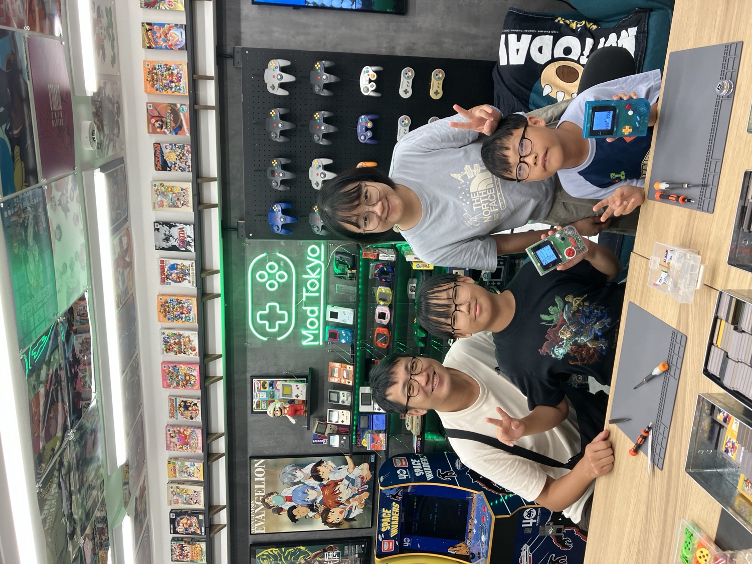 A family of four flashing peace signs with their finished Game Boys under the Mod Tokyo neon sign
