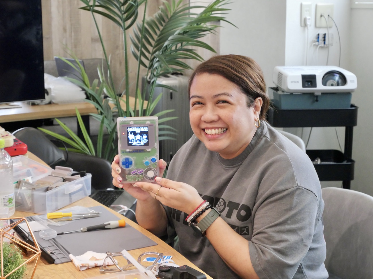 Guest smiling with her finished clear-shell Game Boy, screen lit
