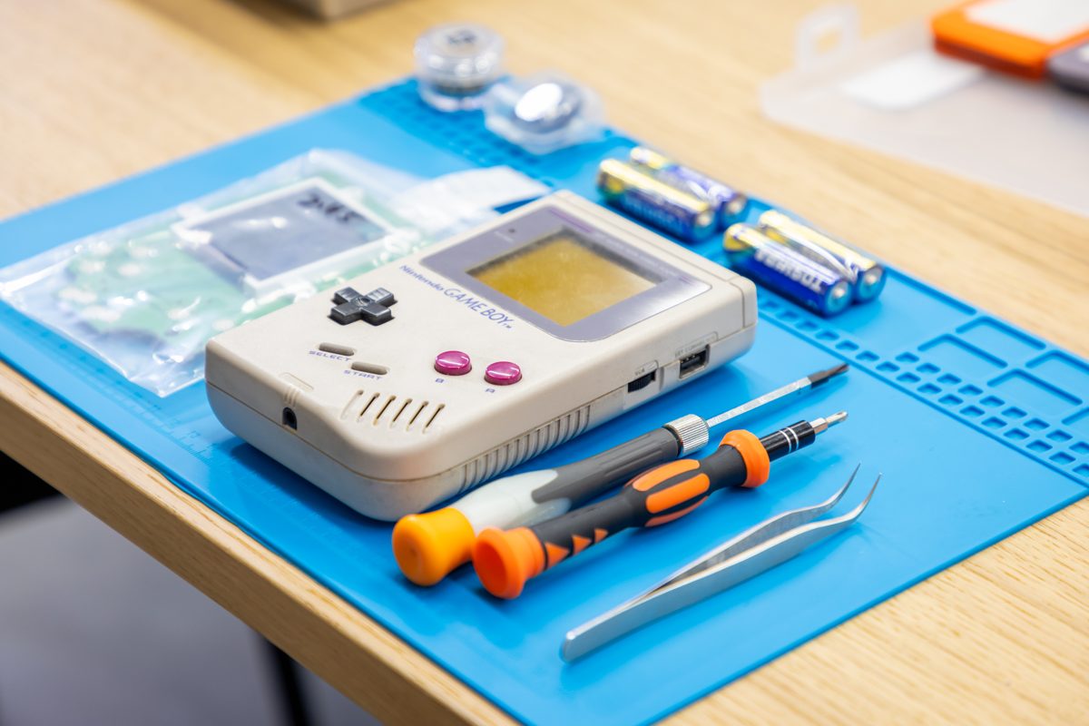 A vintage Game Boy, new parts and tools laid out on the work mat, ready to begin